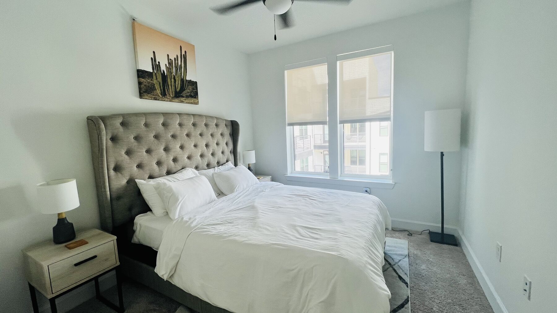 Bedroom with tufted grey wingback headboard, white linens, and a desert cactus canvas print above the bed