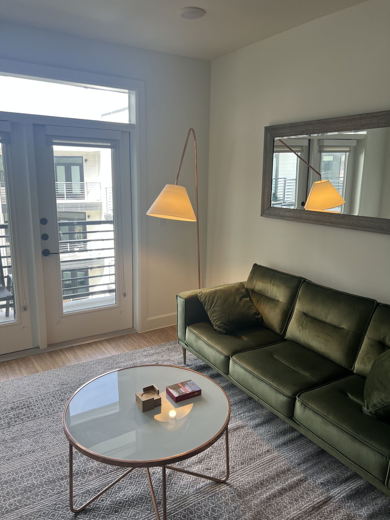 Living room with olive green velvet sofa, brass floor lamp, and round glass coffee table